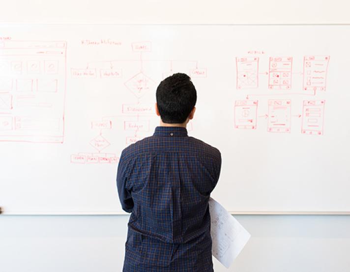 a person stands in front of a whiteboard looking at a sitemap and wireframe