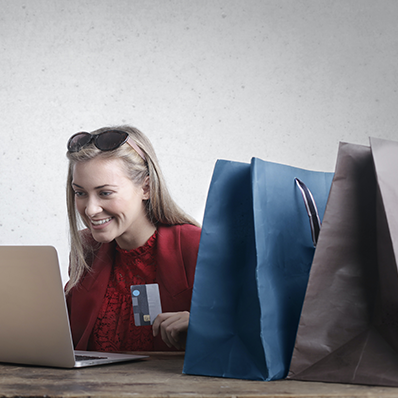 a woman smiles at her computer with shopping bags